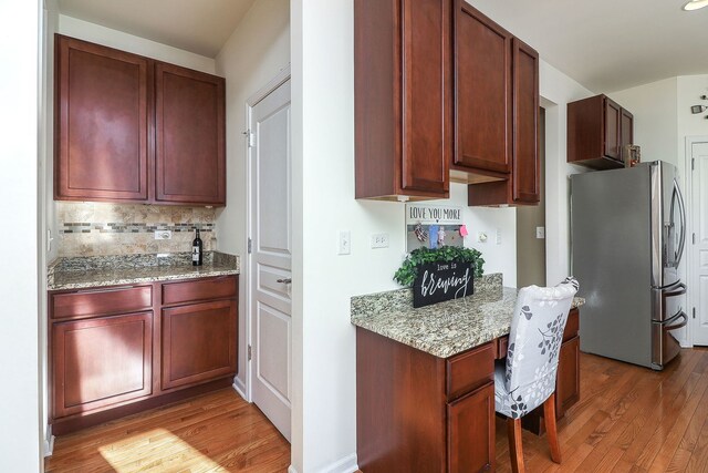 kitchen featuring hardwood / wood-style floors, backsplash, stainless steel refrigerator with ice dispenser, built in desk, and light stone countertops