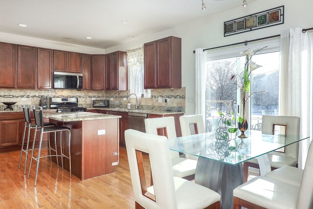 kitchen with backsplash, a kitchen bar, a center island, stainless steel appliances, and light hardwood / wood-style flooring