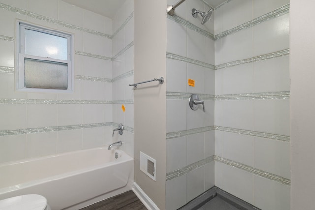 bathroom with hardwood / wood-style flooring, tiled shower / bath, and toilet