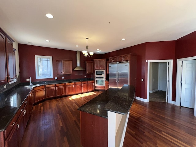 kitchen featuring dark wood-type flooring, built in appliances, a kitchen island, and wall chimney range hood