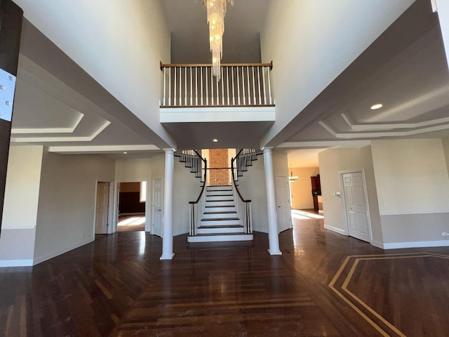 staircase featuring an inviting chandelier, decorative columns, hardwood / wood-style floors, and a high ceiling