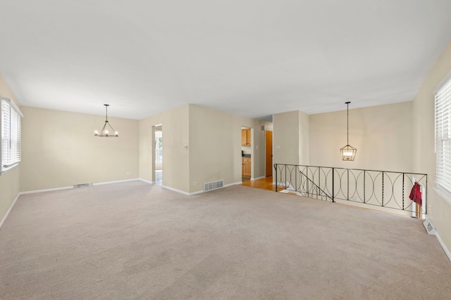 carpeted spare room featuring an inviting chandelier and a healthy amount of sunlight