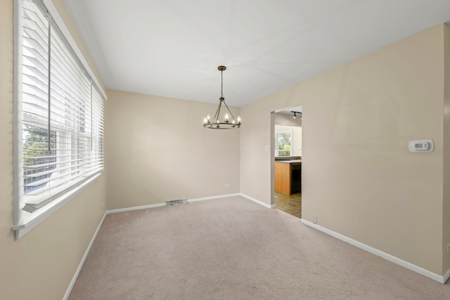 carpeted empty room with an inviting chandelier