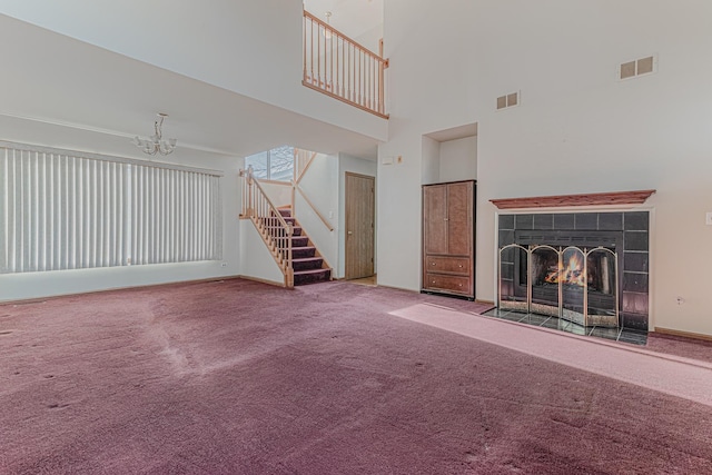 unfurnished living room with a tiled fireplace, a notable chandelier, a towering ceiling, and carpet