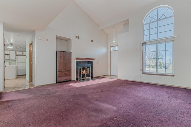 unfurnished living room with high vaulted ceiling, carpet floors, and a tile fireplace