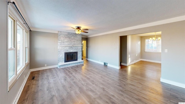 unfurnished living room with hardwood / wood-style flooring, a stone fireplace, ceiling fan with notable chandelier, and a textured ceiling