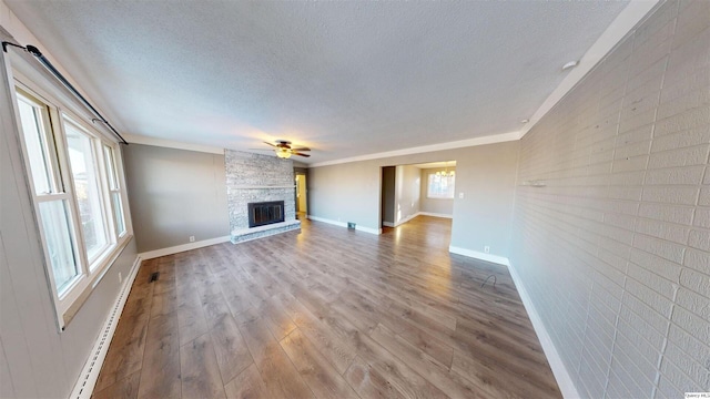 unfurnished living room featuring ceiling fan, baseboard heating, wood-type flooring, a textured ceiling, and a stone fireplace