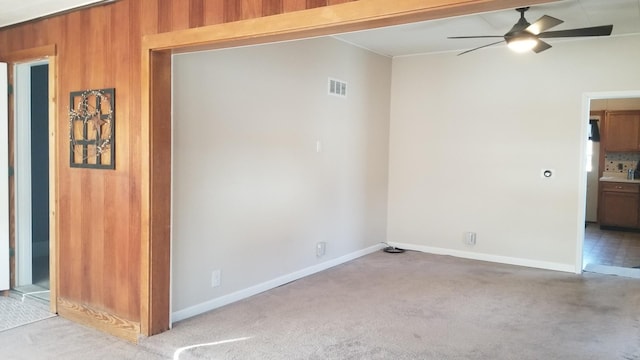 unfurnished room with visible vents, light carpet, ceiling fan, wooden walls, and baseboards