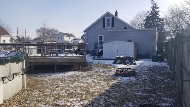 snow covered property featuring an outbuilding, a chimney, a storage shed, a deck, and fence private yard