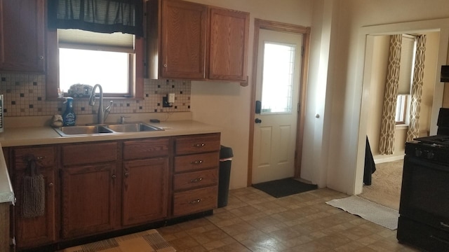 kitchen with light countertops, brown cabinetry, a sink, and black gas stove