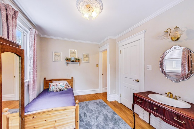 bedroom with baseboards, ornamental molding, a sink, and light wood-style floors