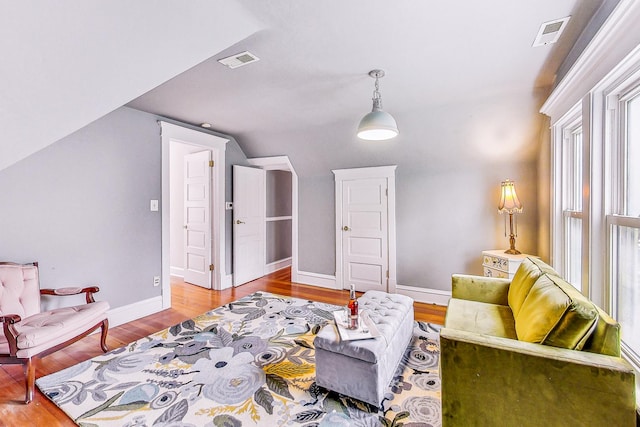 living area featuring baseboards, visible vents, vaulted ceiling, and wood finished floors