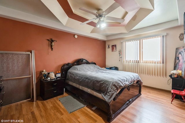 bedroom with ceiling fan, a tray ceiling, and light wood-type flooring