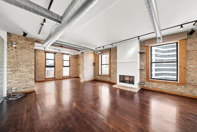 unfurnished living room with brick wall, hardwood / wood-style floors, and plenty of natural light