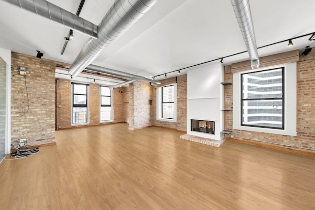 unfurnished living room with wood finished floors, a brick fireplace, brick wall, and track lighting