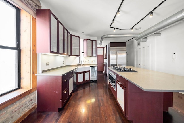 kitchen with dark brown cabinets, dark wood-type flooring, beverage cooler, light countertops, and appliances with stainless steel finishes