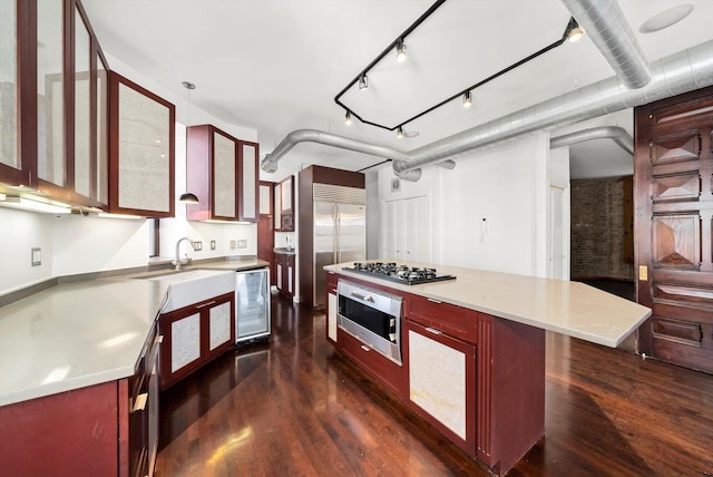 kitchen with a sink, dark wood finished floors, appliances with stainless steel finishes, and reddish brown cabinets