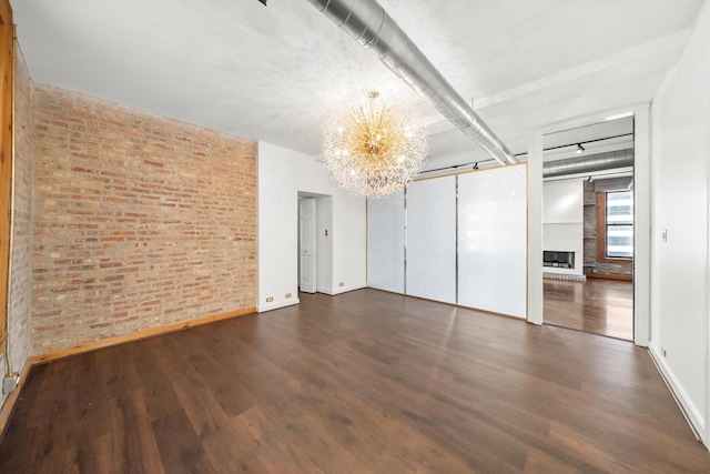 empty room with a barn door, brick wall, dark wood-type flooring, and a chandelier