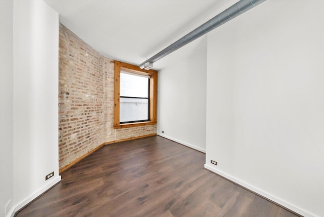 empty room with baseboards, dark wood-type flooring, and brick wall