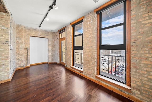 spare room with dark wood-type flooring, track lighting, and brick wall