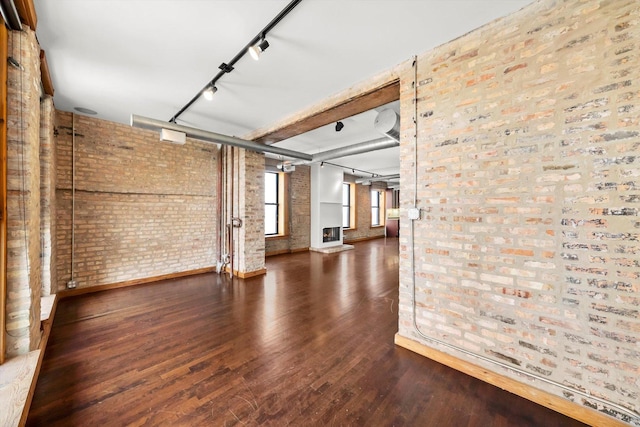 unfurnished room with dark wood-type flooring, track lighting, and brick wall