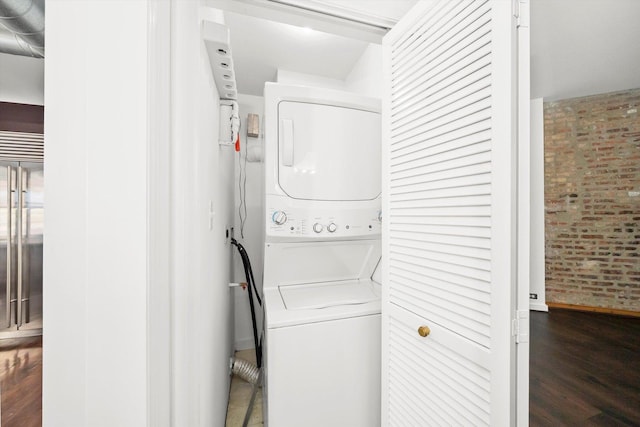 washroom with wood finished floors, stacked washer and clothes dryer, brick wall, and laundry area