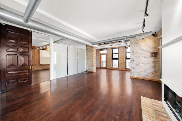 unfurnished living room with dark wood-type flooring, brick wall, and rail lighting