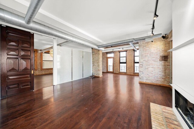 unfurnished living room featuring wood finished floors, brick wall, and track lighting