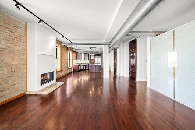 unfurnished living room with a glass covered fireplace, wood finished floors, brick wall, and rail lighting