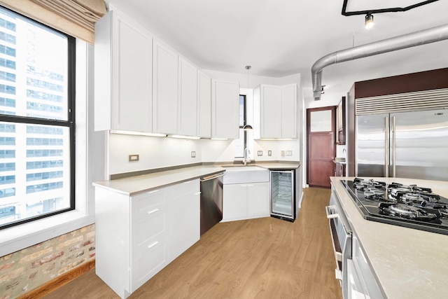 kitchen featuring beverage cooler, light wood-type flooring, white cabinets, stainless steel appliances, and a sink