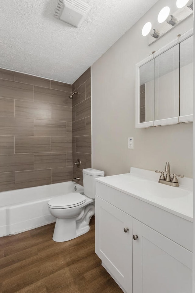 full bathroom featuring tiled shower / bath, hardwood / wood-style flooring, vanity, toilet, and a textured ceiling