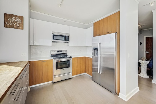 kitchen featuring tasteful backsplash, white cabinets, stainless steel appliances, crown molding, and light wood-type flooring