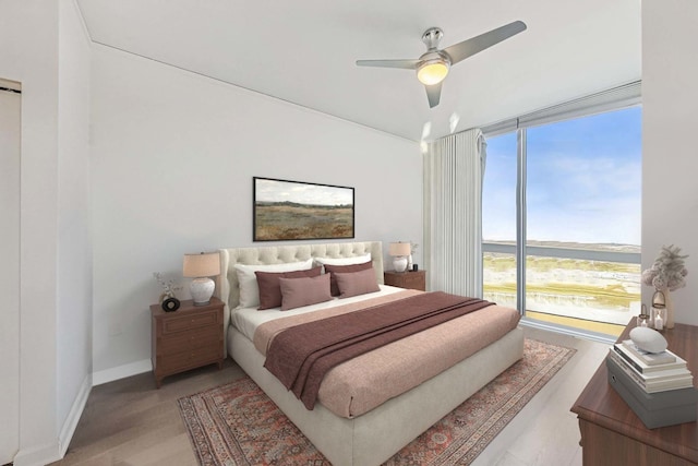 bedroom with light wood-type flooring, floor to ceiling windows, ceiling fan, and a water view