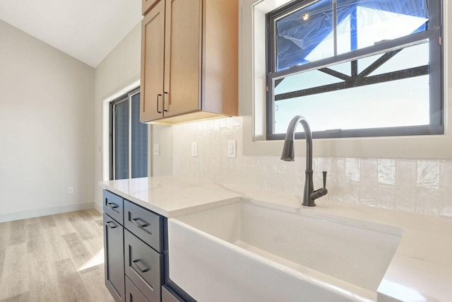 kitchen with vaulted ceiling, tasteful backsplash, sink, light stone counters, and light hardwood / wood-style floors