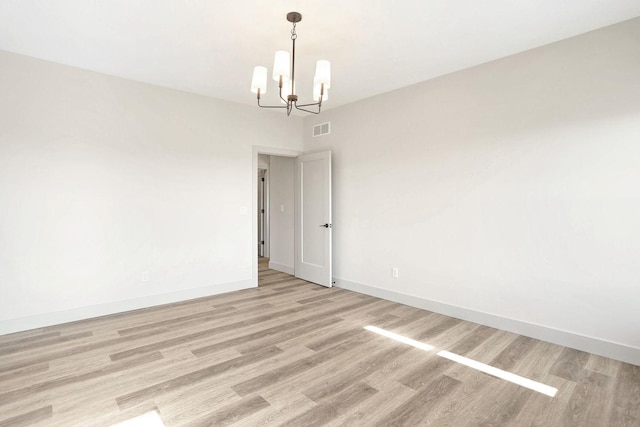 empty room with a notable chandelier and light hardwood / wood-style floors