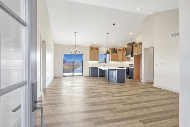 kitchen with a kitchen bar, stainless steel range with electric cooktop, hanging light fixtures, a center island with sink, and a high ceiling