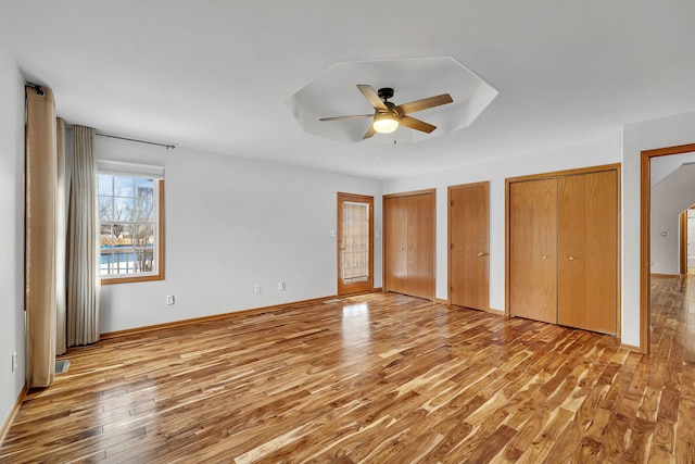 unfurnished bedroom featuring ceiling fan, a raised ceiling, light hardwood / wood-style floors, and two closets