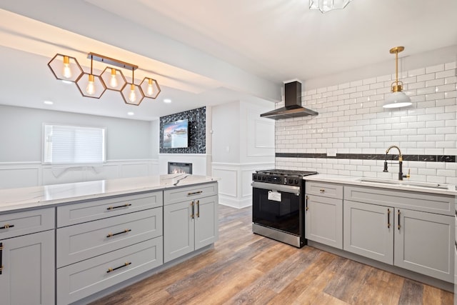 kitchen with gray cabinets, pendant lighting, range with gas cooktop, sink, and wall chimney exhaust hood