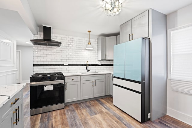 kitchen with gray cabinets, decorative light fixtures, white fridge, wall chimney range hood, and stainless steel gas range