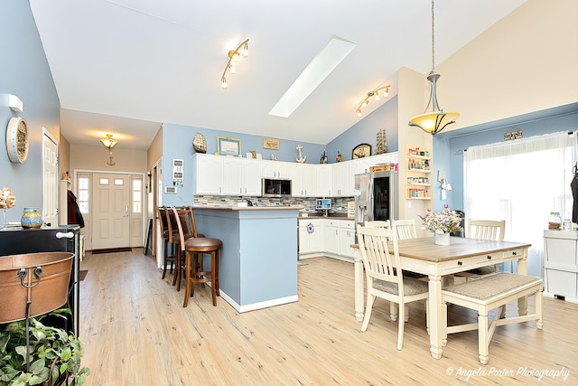 kitchen with appliances with stainless steel finishes, a wealth of natural light, white cabinets, backsplash, and hanging light fixtures