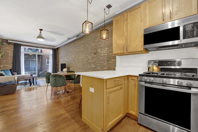 kitchen featuring brick wall, stainless steel appliances, decorative light fixtures, and kitchen peninsula