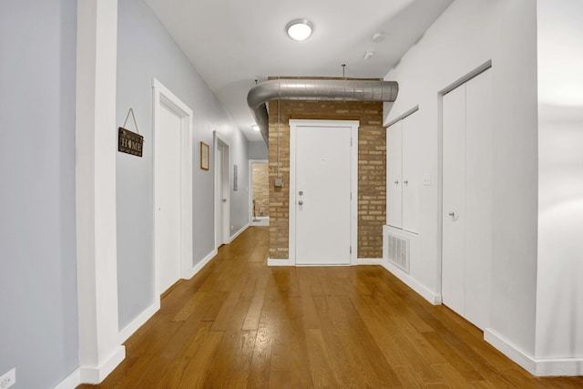 corridor with hardwood / wood-style flooring and brick wall