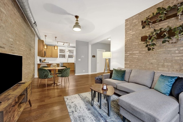 living room featuring brick wall, dark hardwood / wood-style floors, and track lighting