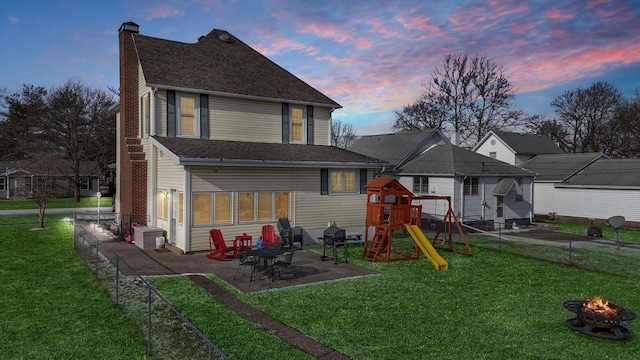 back house at dusk featuring an outdoor fire pit, a yard, a playground, and a patio area