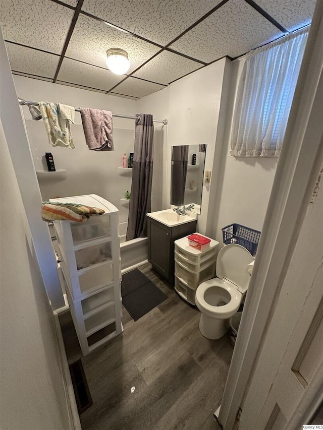 full bathroom featuring toilet, a paneled ceiling, wood-type flooring, and shower / bathtub combination with curtain