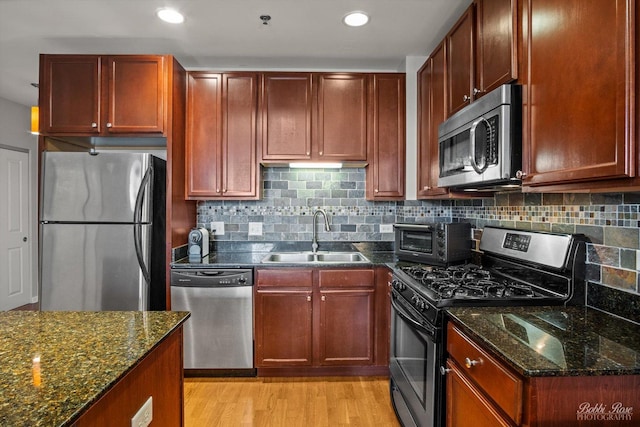 kitchen featuring light wood-type flooring, stainless steel appliances, sink, and dark stone countertops