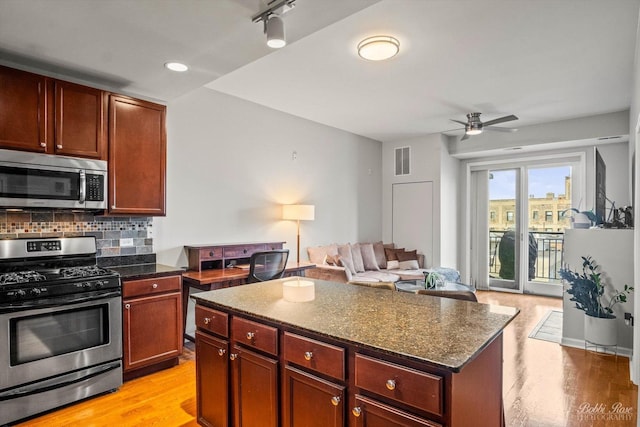 kitchen featuring stainless steel appliances, tasteful backsplash, a kitchen island, dark stone counters, and light wood-type flooring