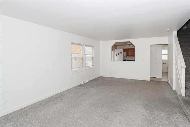 unfurnished living room featuring arched walkways, carpet floors, visible vents, and baseboards