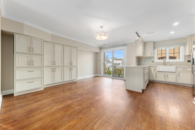 kitchen with tasteful backsplash, sink, hanging light fixtures, light hardwood / wood-style floors, and crown molding