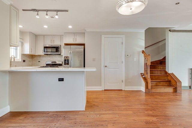 kitchen with crown molding, kitchen peninsula, white cabinets, and appliances with stainless steel finishes